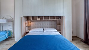 Een slaapkamer met een stapelbed, een groot bed met een blauwe deken, een houten hoofdbord en inbouwplanken.