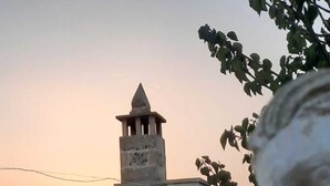 Un edificio de piedra con una torre, mesas al aire libre y una planta de cactus.