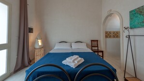 Un dormitorio con cama, una silla, una lámpara, un ventanal con cortinas y una pared decorada con azulejos.