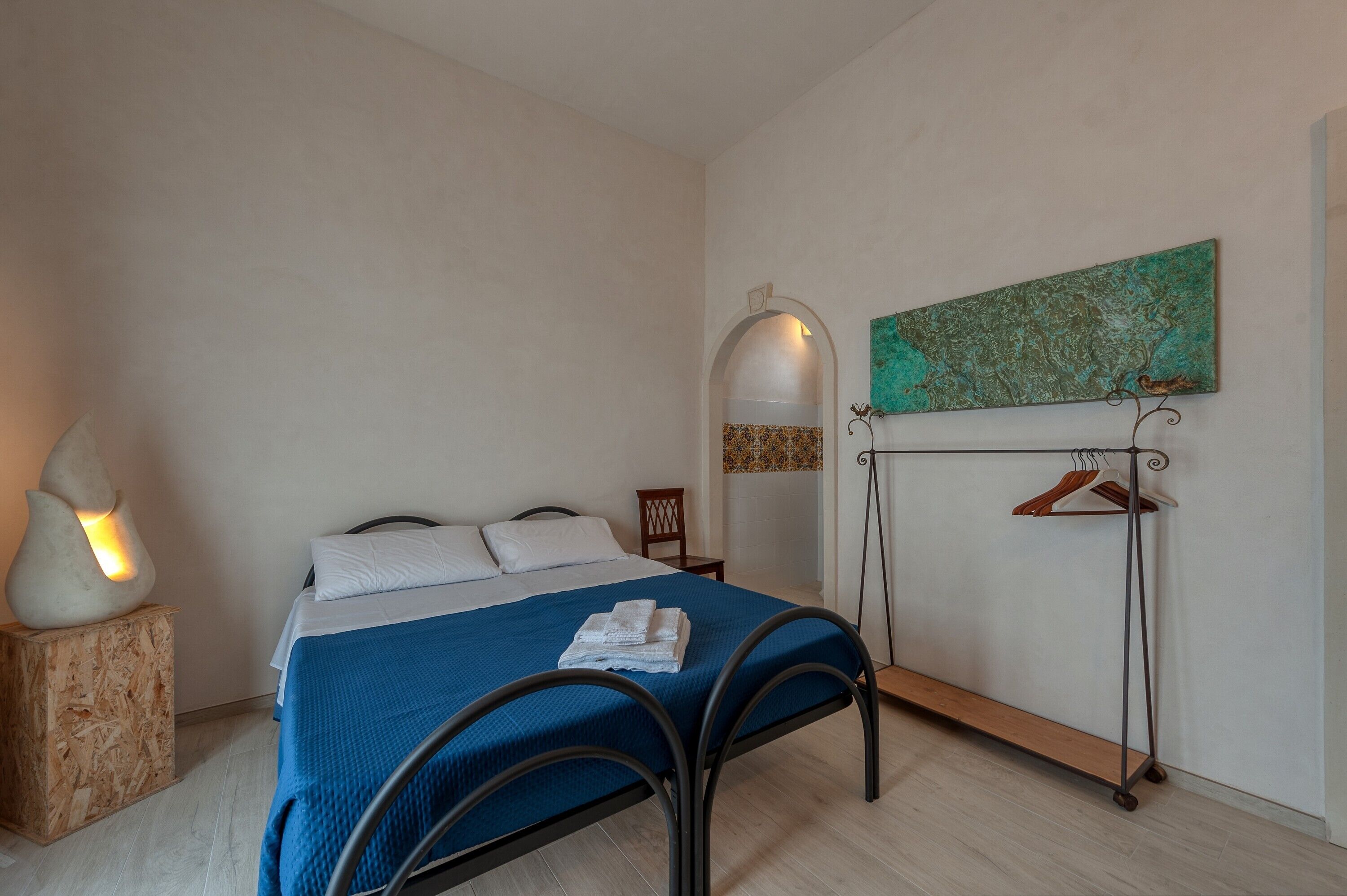 A bedroom with a bed, a nightstand, a wall-mounted coat rack, and a decorative wall piece.