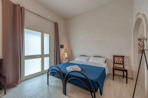 Un dormitorio con cama, una silla, una lámpara y una ventana.