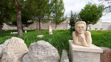 A sculpture of a reclining figure on a pedestal, surrounded by rocks and grass, with trees and a building in the background.