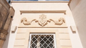 Fachada de edificio con un escudo decorativo, una ventana con diseño de cuadrícula y cielo despejado.