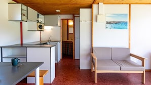 Een ruimtelijke leefruimte met een kitchenette, een eethoek, een bank en een schilderij van een kustlandschap.