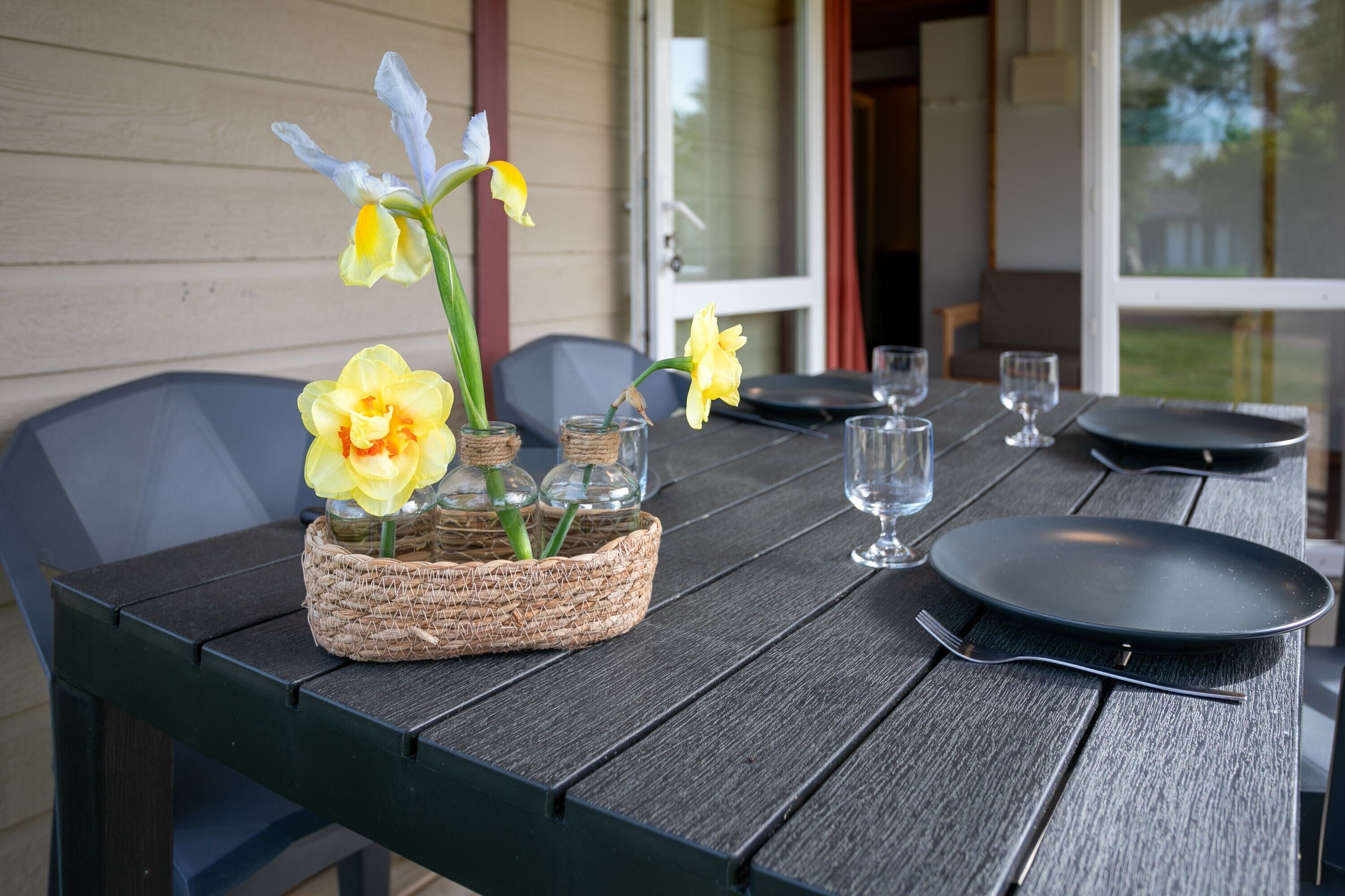 Una mesa de comedor con una cesta tejida que contiene flores, un plato y cubiertos.