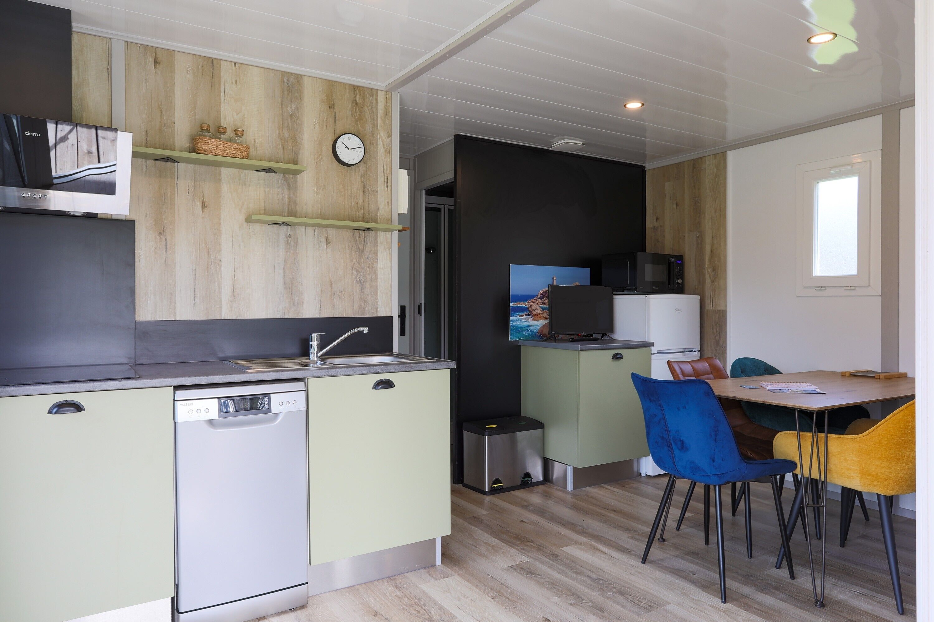 A compact kitchen with a dishwasher, microwave, and a small dining area with chairs.