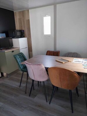 Un coin repas comprenant une table en bois, deux chaises, un petit réfrigérateur et un four à micro-ondes.