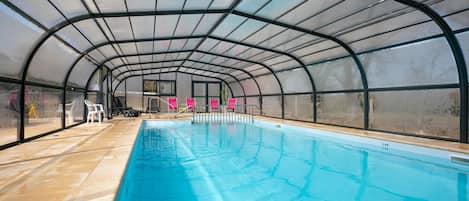 An indoor swimming pool with a glass ceiling, clear water, and a tiled floor.
