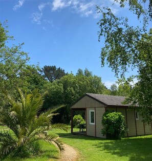 A small, single-story building with a porch, surrounded by lush greenery and trees.