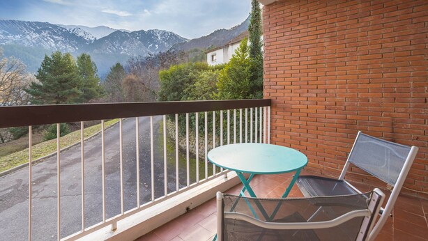 Un balcon avec une table et une chaise, un mur en briques et une vue sur la montagne.