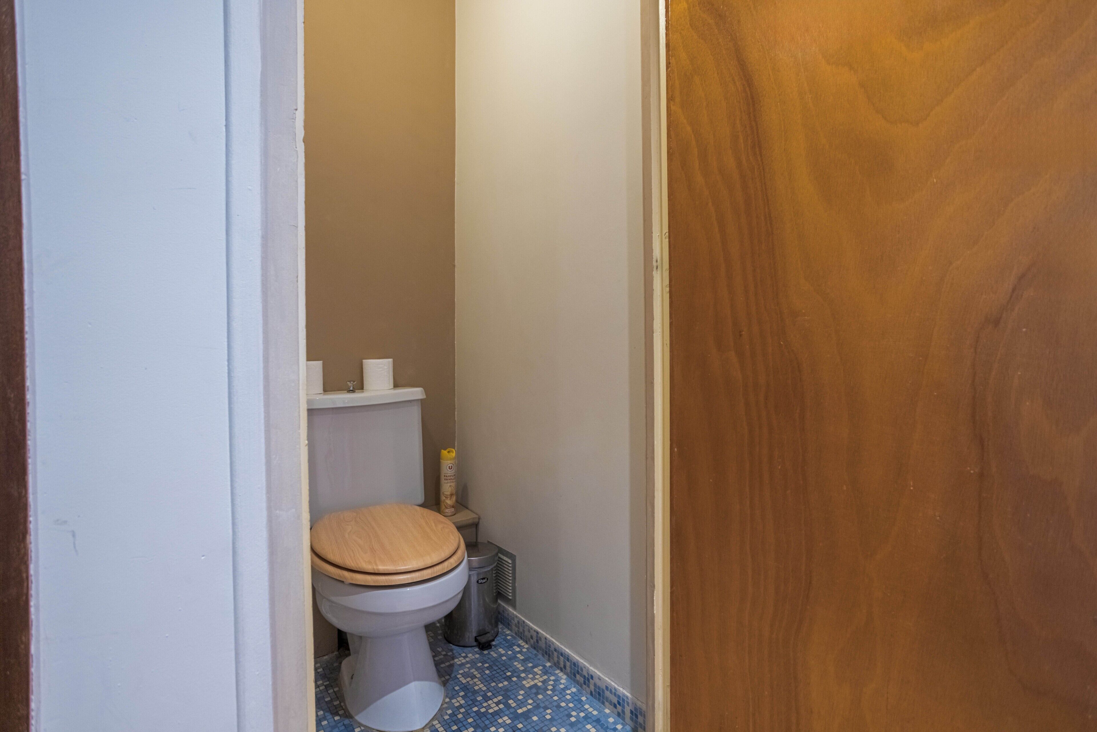 A small bathroom with a toilet, a trash bin, and a toilet paper holder.