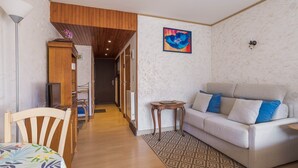 Un salon avec un canapé, une chaise en bois, une petite table et un téléviseur.