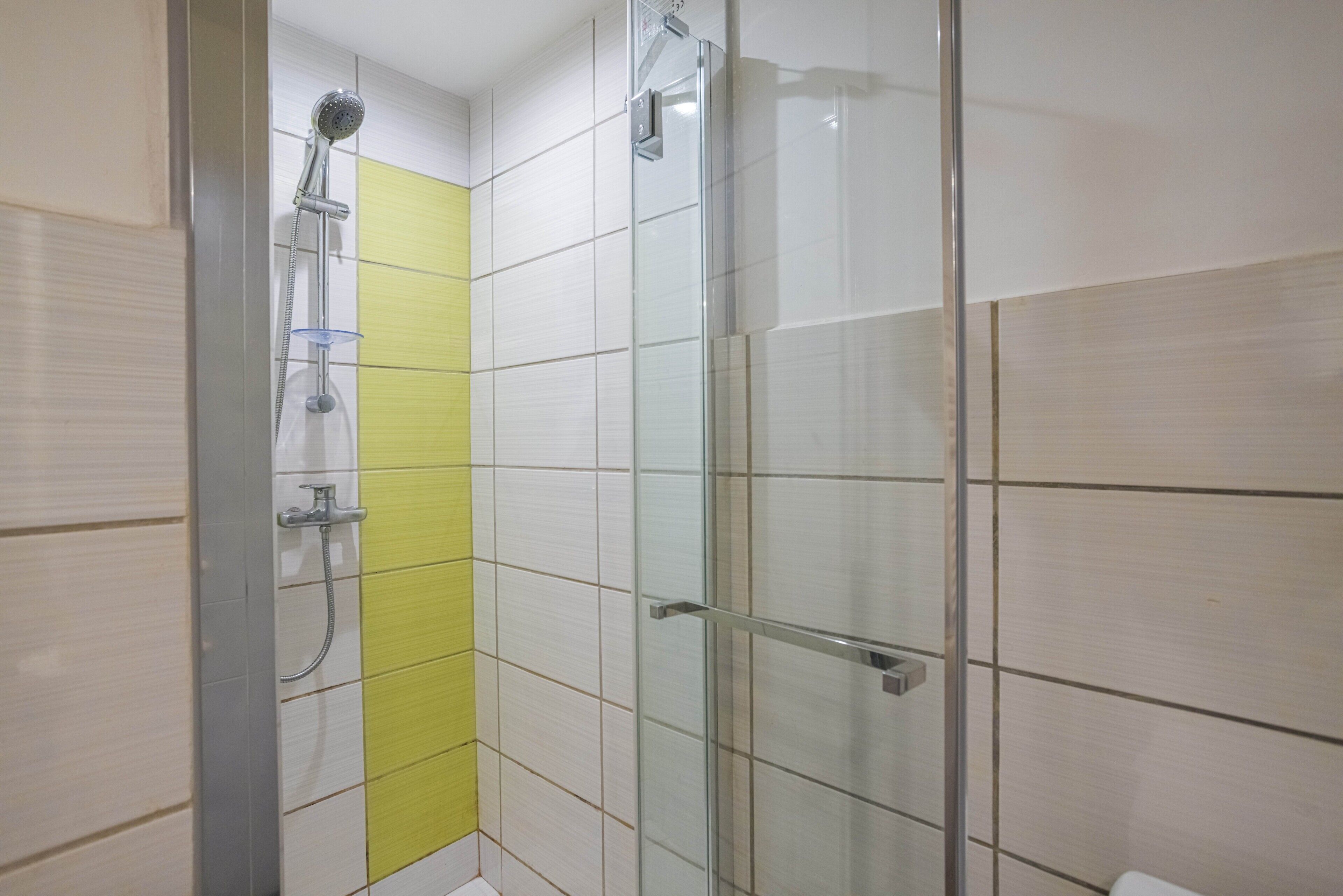 A shower with a glass door, a yellow vertical stripe on the wall, and a tiled floor.