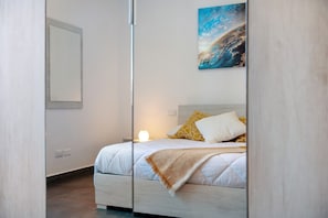 Un dormitorio con cama, mesita de noche, lámpara y un cuadro en la pared.
