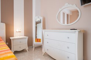 A bedroom with a bed, a dresser, a nightstand, a mirror, and a television mounted on the wall.
