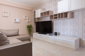 A modern living room with a flat-screen TV, a sofa, a cabinet with shelves, and a patterned wallpaper.