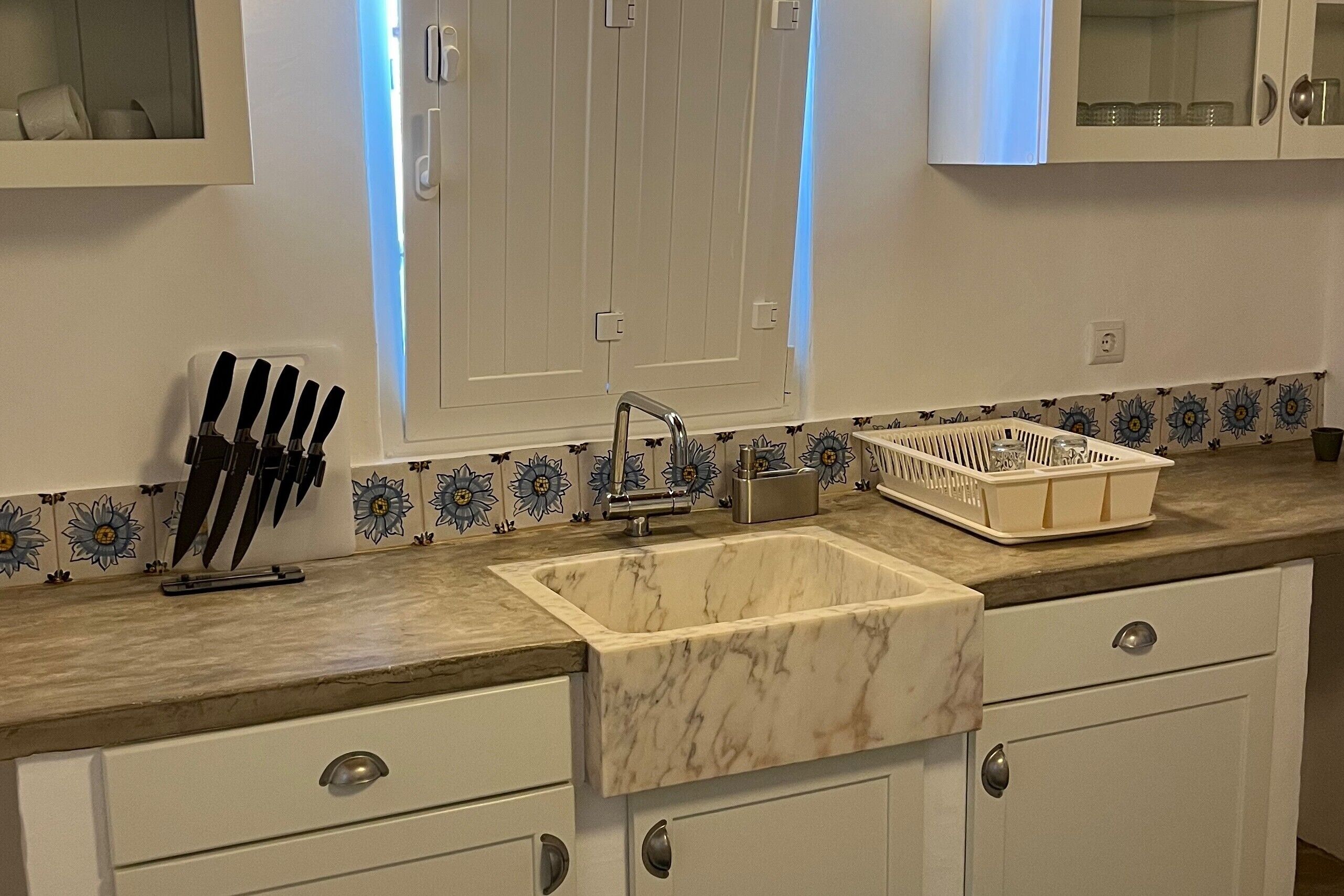 A kitchen with a marble sink, white cabinets, a knife block, and a patterned backsplash.