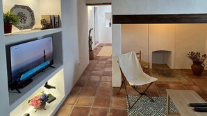 Ein modernes Interieur mit Fernseher auf einer Ablage, einem Essbereich mit Tisch und Stühlen sowie einem gemusterten Teppich.