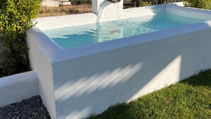 Ein Schwimmbecken mit weißer Struktur, umgeben von Gras und Bäumen, mit Blick auf Häuser im Hintergrund.
