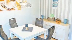 A dining area with a white table, grey upholstered chairs, a hanging light fixture, and a striped wall with a sign. - Koje 44 by Interhome (Damp)