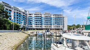 A marina with boats docked, a modern building with blue and white facade, and a clear sky. - Koje 44 by Interhome (Damp)