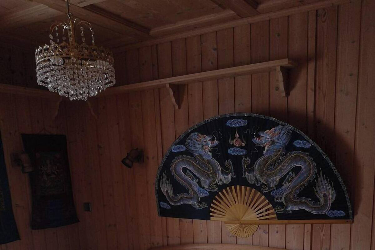 A wooden cabin room with two beds, each with a pillow and a rolled towel. A decorative fan and a chandelier are visible on the wall.