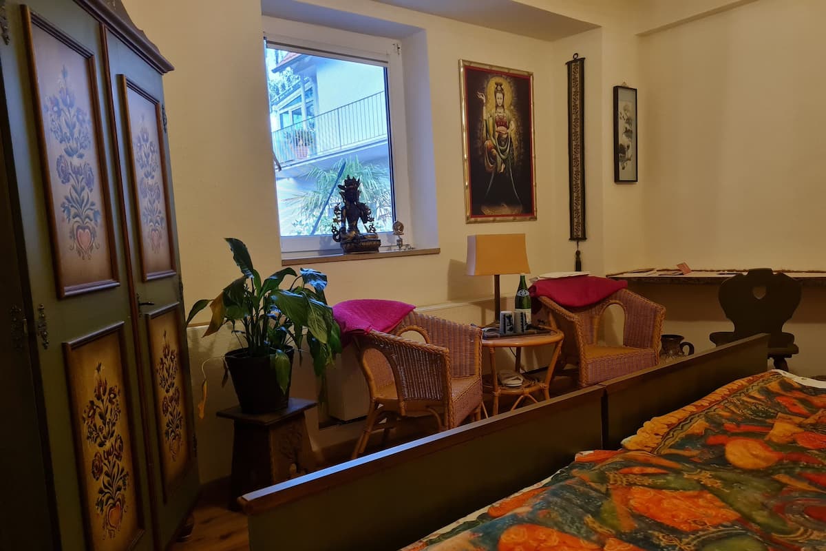 A bedroom with a bed, a desk, a chair, a window, and a potted plant.