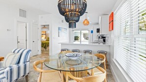 Una cucina moderna con mobili bianchi, un'area pranzo con tavolo in vetro e un'ampia finestra con persiane.
