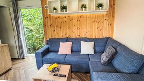 A modern living room with a blue sectional sofa, a wooden wall panel, and a small shelf with plants.