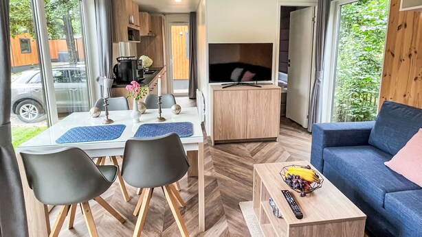 A modern, well-lit living area with a dining table, chairs, a sofa, and a TV.