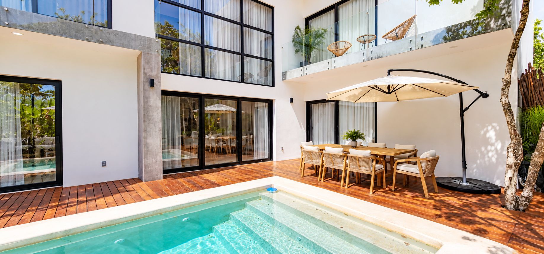 A modern outdoor pool area with a wooden deck, a dining set, and a large umbrella.