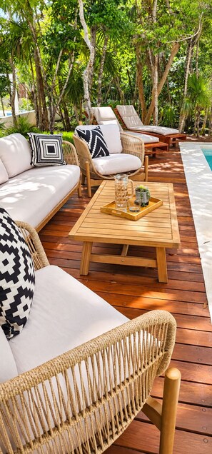A wooden deck with a sofa, two lounge chairs, and a table with a tray.