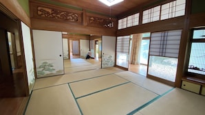 Ein traditioneller japanischer Raum mit Tatami-Böden, Schiebetüren und Blick auf einen Garten.