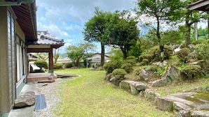 Ein traditioneller japanischer Garten mit einem Kiesweg, einer Holzhütte und üppiger Vegetation.