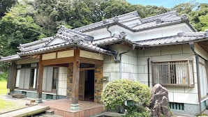 Ein traditionelles japanisches Gebäude mit einem Ziegeldach, Holzbalken und einem kleinen Garten mit Stein und Strauch.
