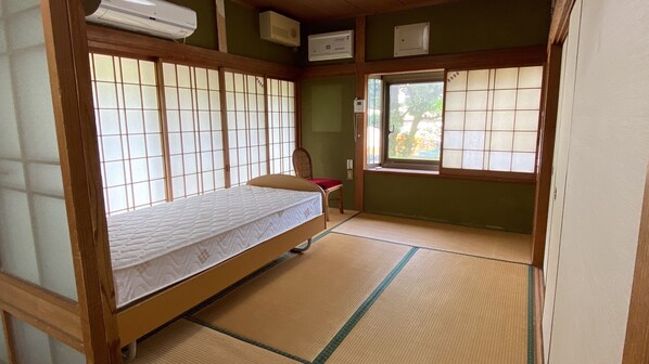 Una habitación japonesa tradicional con suelo de tatami, futón, puertas correderas shoji y vistas por una ventana.