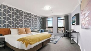A hotel room with a bed, a desk, a chair, a window, and a view of the city. - KozyGuru | Haymarket | Chic City Studio (Haymarket)