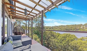 A covered outdoor seating area with a view of a bridge and greenery. - KozyGuru | Waterfront Holiday House (Padstow Heights)