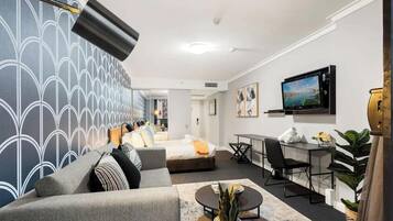 A modern hotel room with a bed, sofa, desk, TV, and a view of the city.