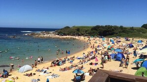 Ein überfüllter Strand mit Menschen, die sonnenbaden und schwimmen, Zelten und Sonnenschirmen.