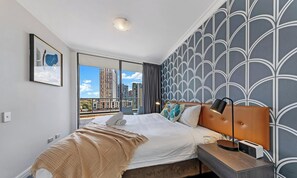 Una camera d'albergo moderna con un letto grande, una testiera, un comodino con una lampada, un quadro appeso al muro e vista sulla città.