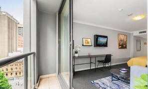 A modern apartment with a balcony, a dining area with a table and chairs, and a living area with a sofa and a TV.