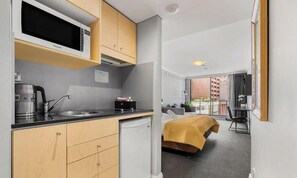 Angolo cottura compatto con forno a microonde, bollitore e lavello, un letto con coperta gialla e un balcone con vista.