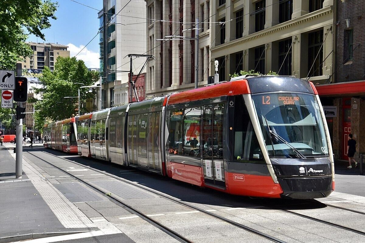 A modern tram with the number 12 on its front, traveling on a track in an urban setting.