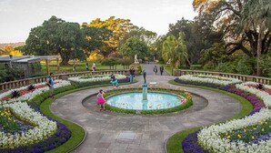 A garden with a central fountain, surrounded by flower beds and pathways. - KozyGuru | Sydney CBD | High Level 2 Bed Studio (Haymarket)