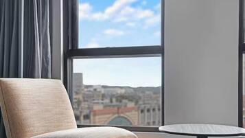 A room with a view of a cityscape through a window, a chair, and a small round table.