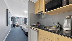 A hotel room with a kitchenette, a bed, a desk, and a view of the city. - KozyGuru | Sydney CBD | High Level 2 Bed Studio (Haymarket)