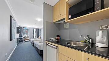 A hotel room with a kitchenette, a bed, a desk, and a view of the city.
