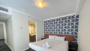 Ein Hotelzimmer mit Bett, Nachttisch, Wand mit geometrischem Muster, Deckenleuchte und Tür zu einem Badezimmer.