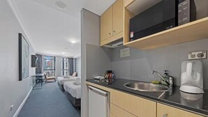 Une chambre d’hôtel moderne équipée d’une kitchenette, d’un lit, d’une petite table et offrant une vue sur la ville.